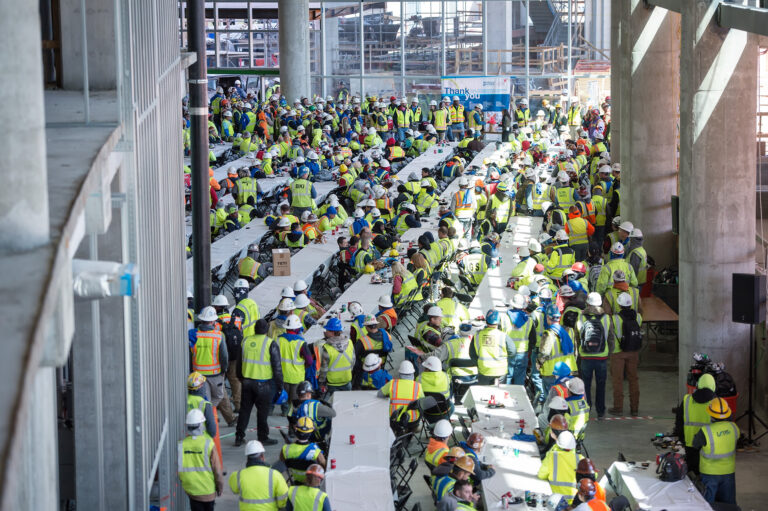 Large group of construction workers in high-visibility vests gathered for a Topping Out Milestone meeting inside the spacious Piedmont Atlanta Tower industrial site.