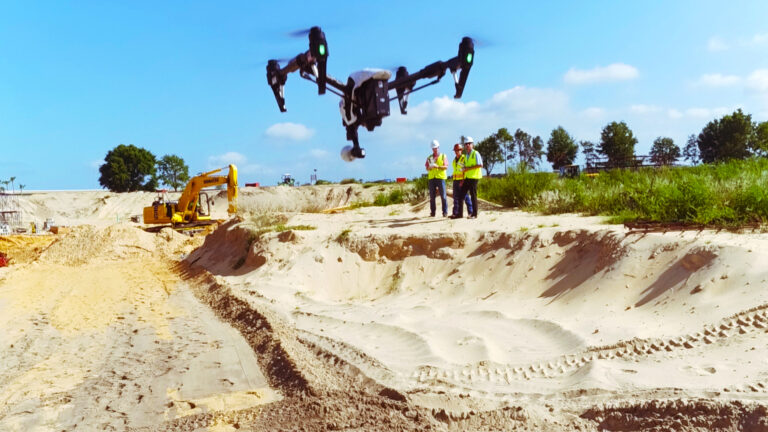 Construction professionals implementing innovation by operating a drone at a construction site with heavy machinery in the background.