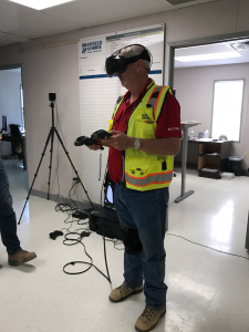 Man in a high-visibility vest successfully implementing construction technologies using virtual reality equipment in an office setting.