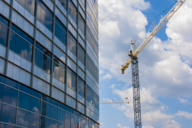 Glass facade of a skyscraper with a construction crane against a cloudy sky.