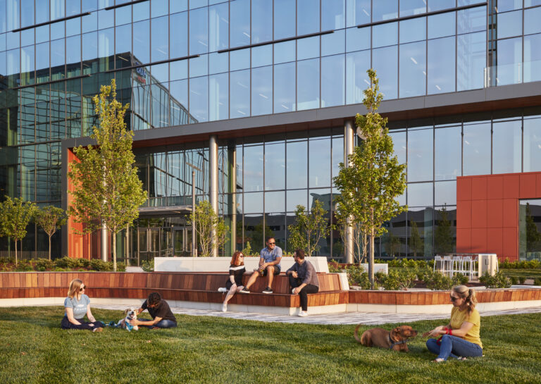 People relaxing and working outdoors on a sunny day near a modern office building.