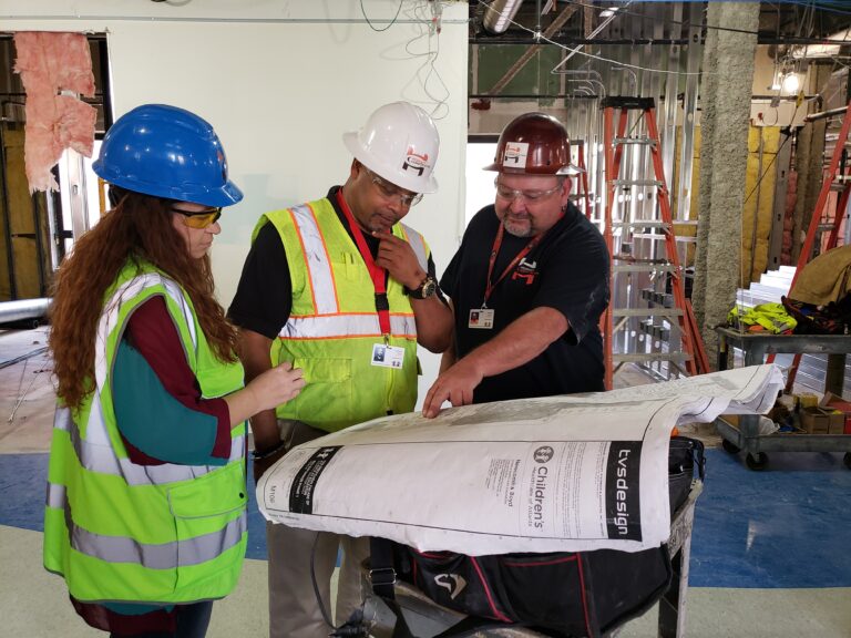 Three diverse construction professionals from WEBMyers Construction reviewing blueprints at a job site.