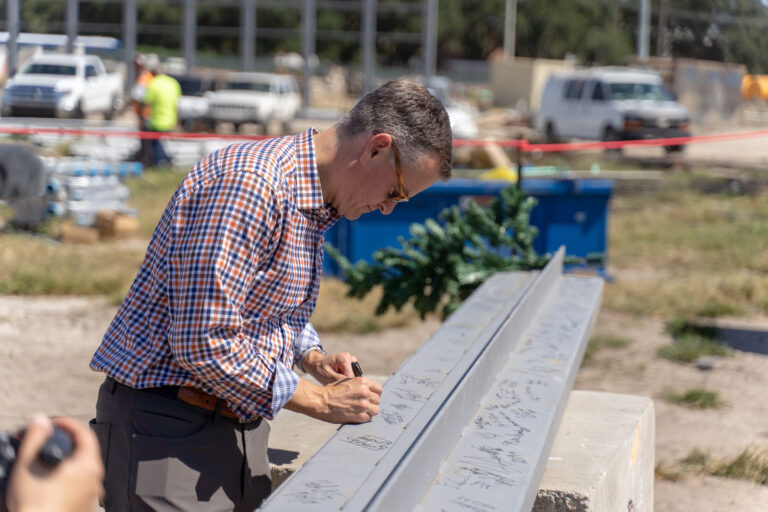 Man signing his name on a steel beam at a construction site.