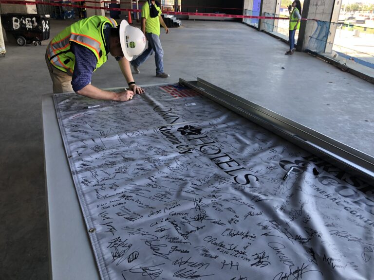 Construction worker signing a steel beam covered with signatures before it is installed in a building.