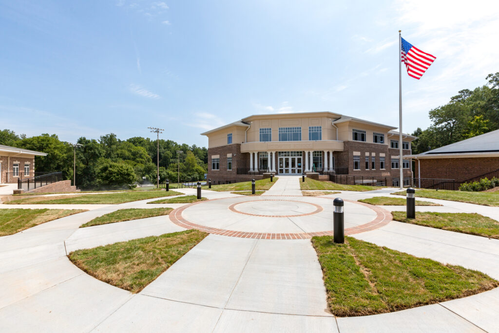 A modern educational building, a Brasfield & Gorrie Project, with an American flag fluttering in the front courtyard under a clear blue sky.
