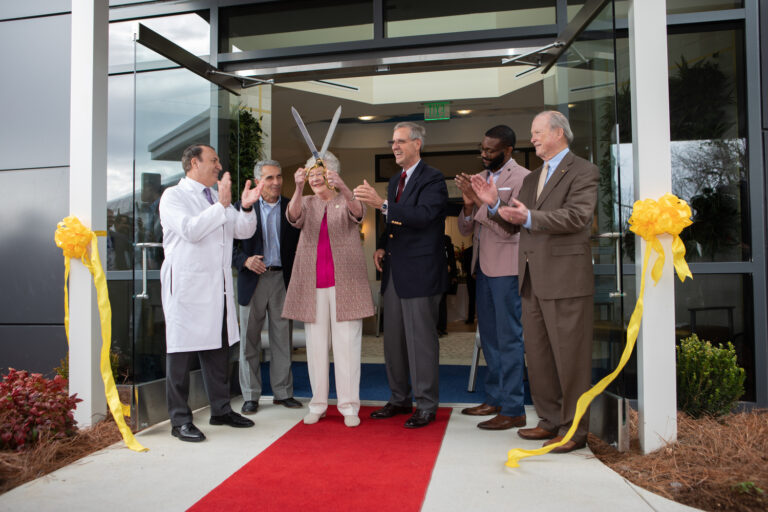 Ribbon-cutting ceremony at Swaid Vestavia Medical Center with a group of individuals, one holding oversized scissors, outside the building entrance.
