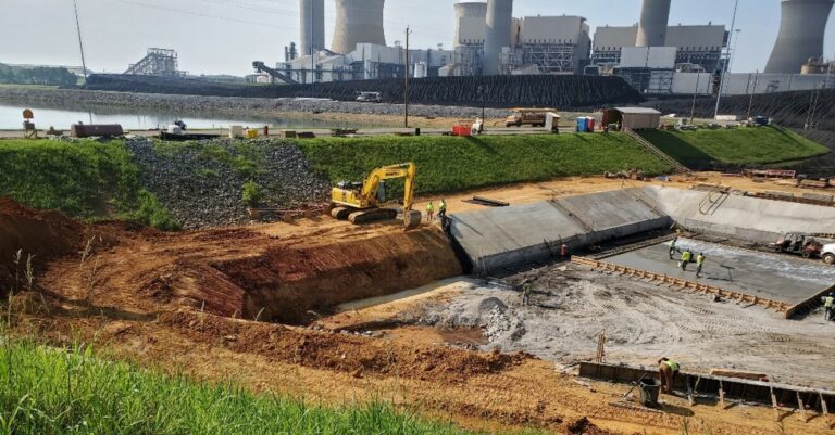 Construction work, advancing automation, is in progress near a power plant with workers and heavy machinery on site.