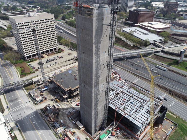 Aerial view of a construction site with a tall structure, adjacent buildings, and nearby roadways, showcasing the theme 