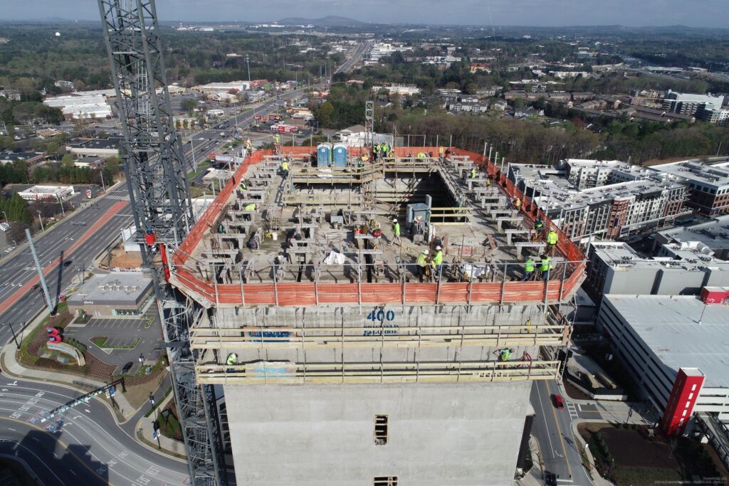 Aerial view of a construction site with workers reaching new heights on top of a partially completed building structure.