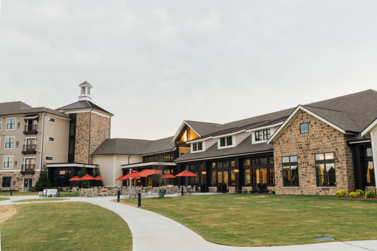 Modern Senior Living Project with a stone facade and outdoor seating area with red umbrellas.