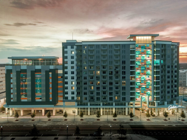 Modern apartment building at Orlando's Creative Village, now open with illuminated windows and ground-floor commercial spaces named Julian Apartments.