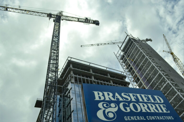 Construction site with cranes and a building under construction, now topping out at Three Ballpark Center, featuring a sign for Brasfield & Gorrie general contractors.