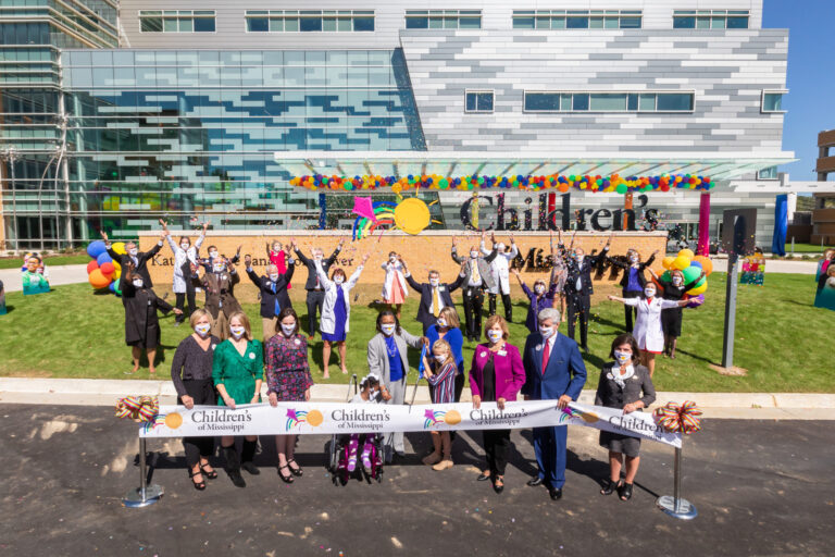 Group of individuals participates in a ribbon-cutting ceremony at the opening of a children's hospital.