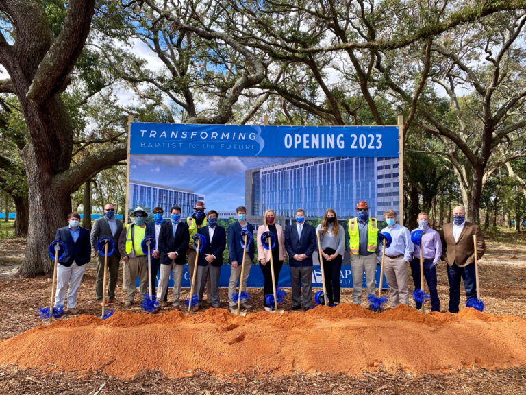 Group of individuals at a groundbreaking ceremony with shovels, standing before a sign that reads 