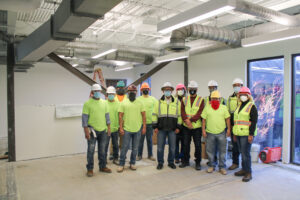 Group of construction workers in high-visibility shirts with hard hats, equipped with the necessary tools, standing together inside a building under construction.