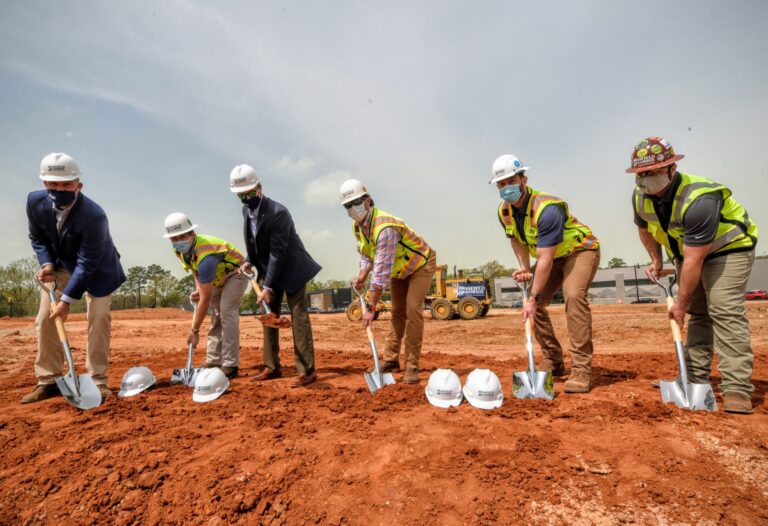 Group of individuals in hard hats and high-visibility vests from Brasfield & Gorrie participating in a groundbreaking ceremony at the WestLawn at BullStreet construction site.