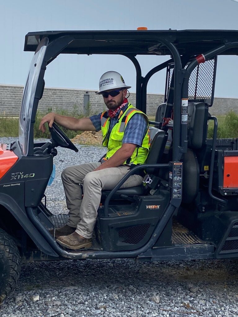 A construction worker wearing a hard hat and a high-visibility vest, embodying the challenging construction career, sitting in a utility vehicle.