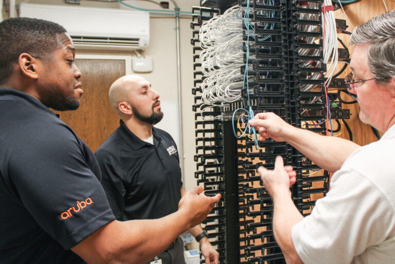 Three technicians working on cable management in a server room to enhance jobsite connectivity for Brasfield & Gorrie.