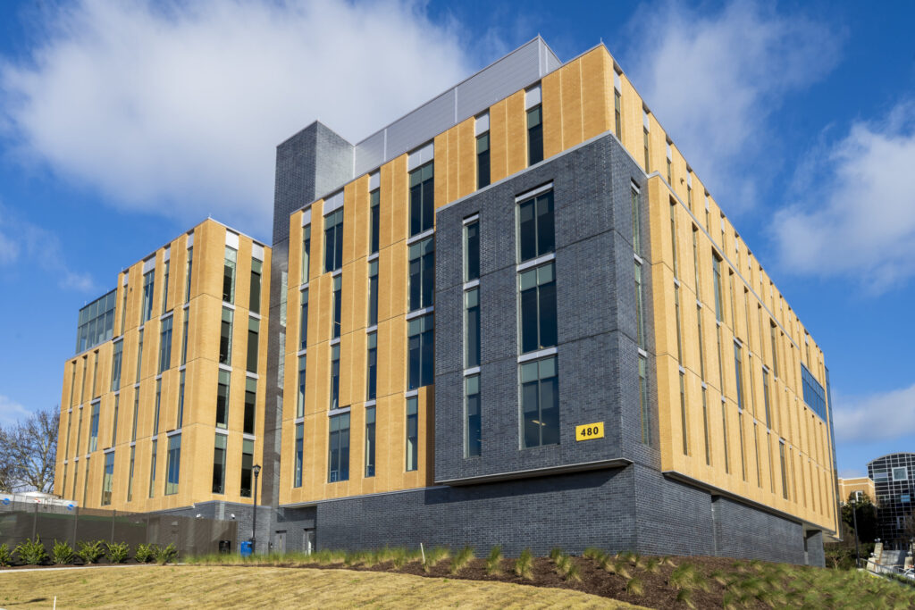 Modern multi-story building part of the Georgia University System with a combination of yellow cladding and grey brickwork, set against a blue sky with clouds.