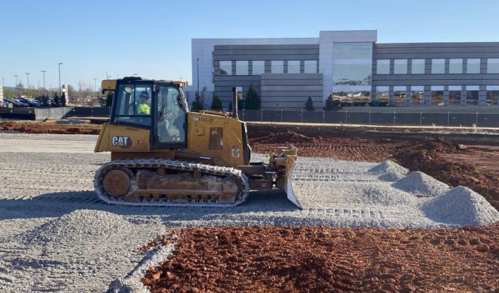 A bulldozer on a construction site with piles of gravel and a building in the background for the HudsonAlpha Institute Expansion Project.
