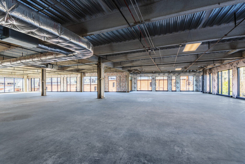 Empty industrial-style office space with exposed ductwork and large windows, ideal for a Lab Conversion.