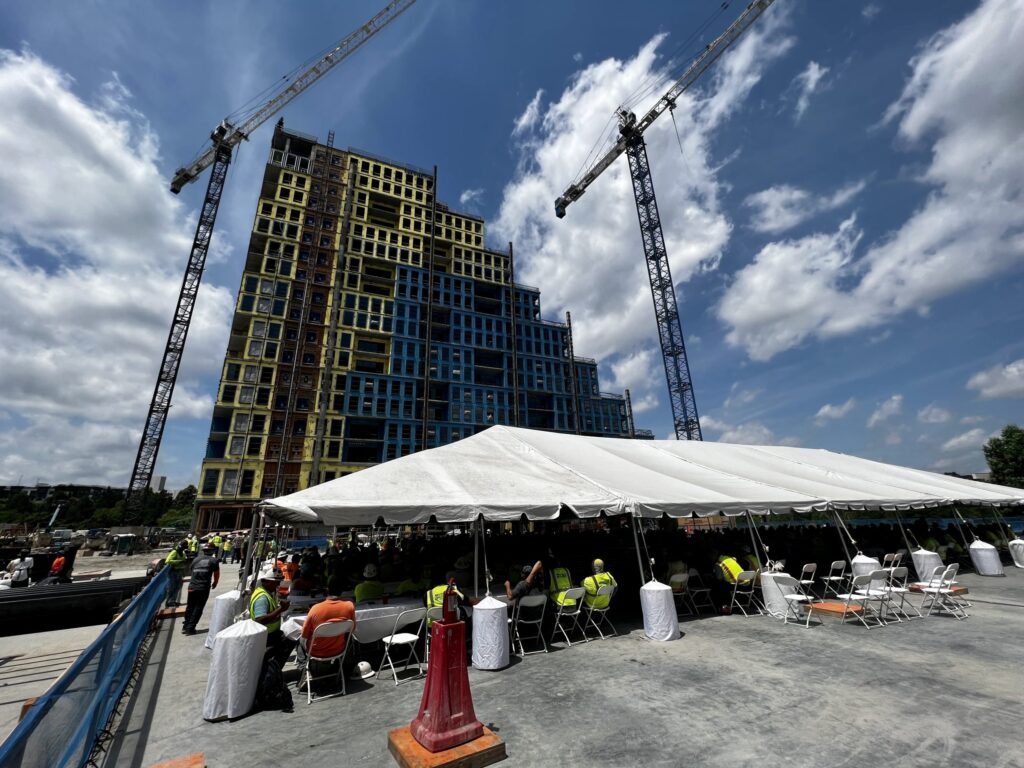 Construction workers gathered under a tent for the "Tops Out" event with a residential tower at 760 Ralph McGill under construction in the background.