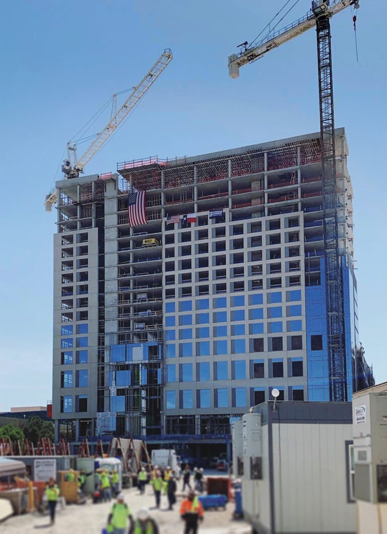 Construction workers in safety vests at a Brasfield & Gorrie building site with cranes and a partially completed high-rise commercial real estate market project displaying an American flag.