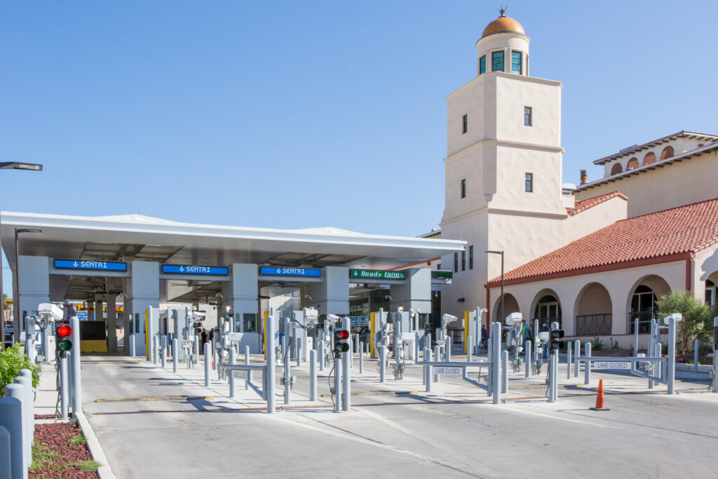 A modern toll booth station with multiple lanes and electronic signs, employing sustainable construction practices, is located near a LEED-certified building with a tower.