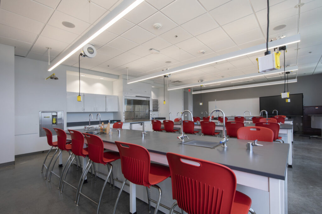 A modern, well-equipped science laboratory at the Alabama School of Cyber Technology and Engineering with red chairs and multiple workstations.