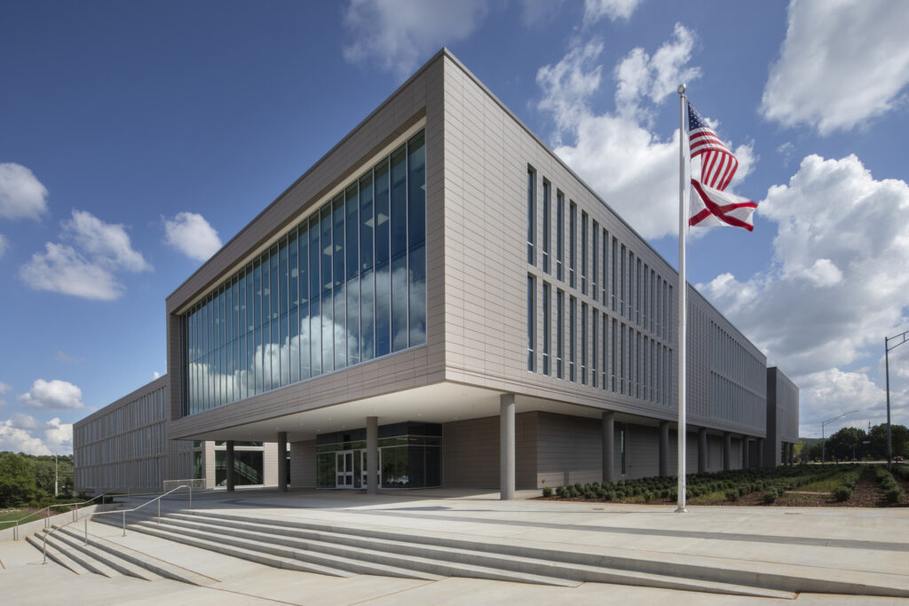 Modern office building with large glass windows and the Alabama School of Cyber Technology and Engineering flag flying at the front.