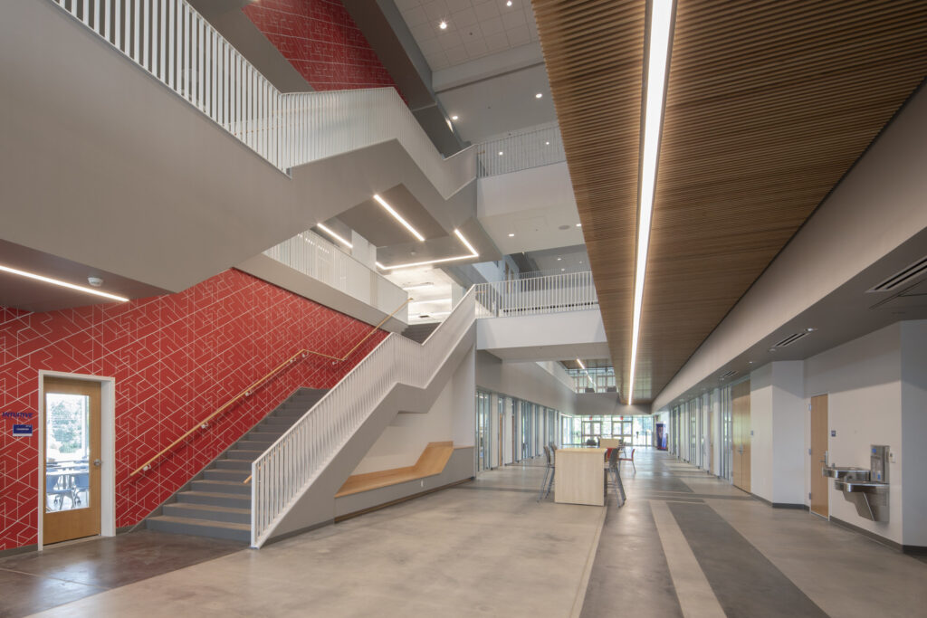 Modern interior of the new campus of the Alabama School of Cyber Technology and Engineering, showcasing a staircase with red tiles and wooden accents.
