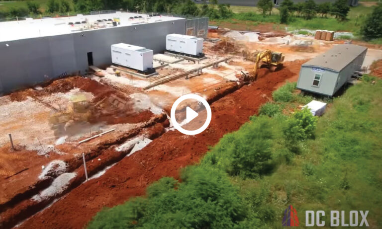 Construction site with excavation work near a large building in Huntsville, with heavy machinery and temporary structures visible for the 20 Megawatts DC BLOX facility.