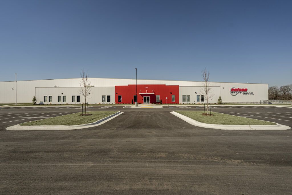 Modern industrial warehouse with red entrance and empty parking lot, serving as a Brasfield & Gorrie Manufacturing Facility in Arkansas.