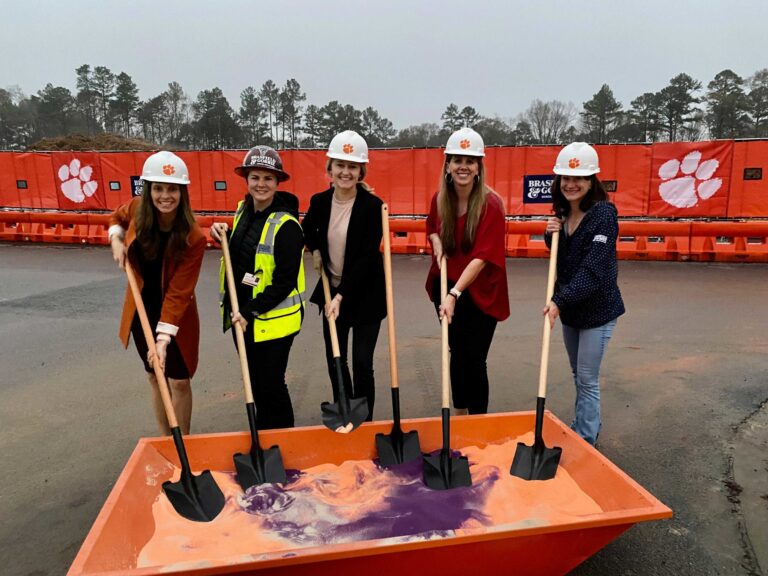 Five individuals in hard hats posing with shovels at a ground breaking ceremony for the Clemson Athletic Facilities.