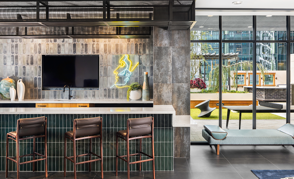 Modern office lounge area in Midtown Union, Atlanta, with a bar, high stools, neon art on the wall, and a view to an outdoor courtyard.