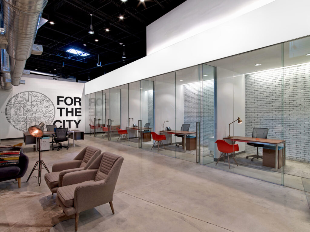 Modern office space with glass walls, individual workstations for developers, and a casual seating area.