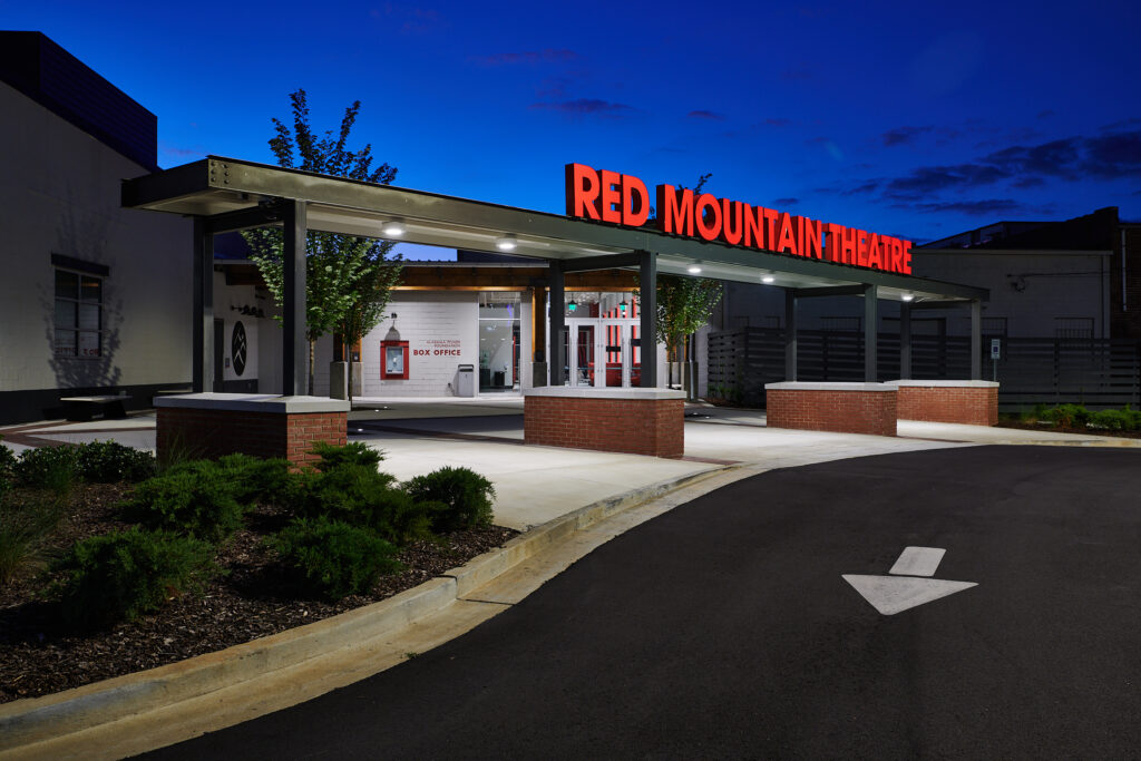 Exterior of red mountain theatre at twilight with illuminated signage, showcasing opportunities for developers in converted spaces.