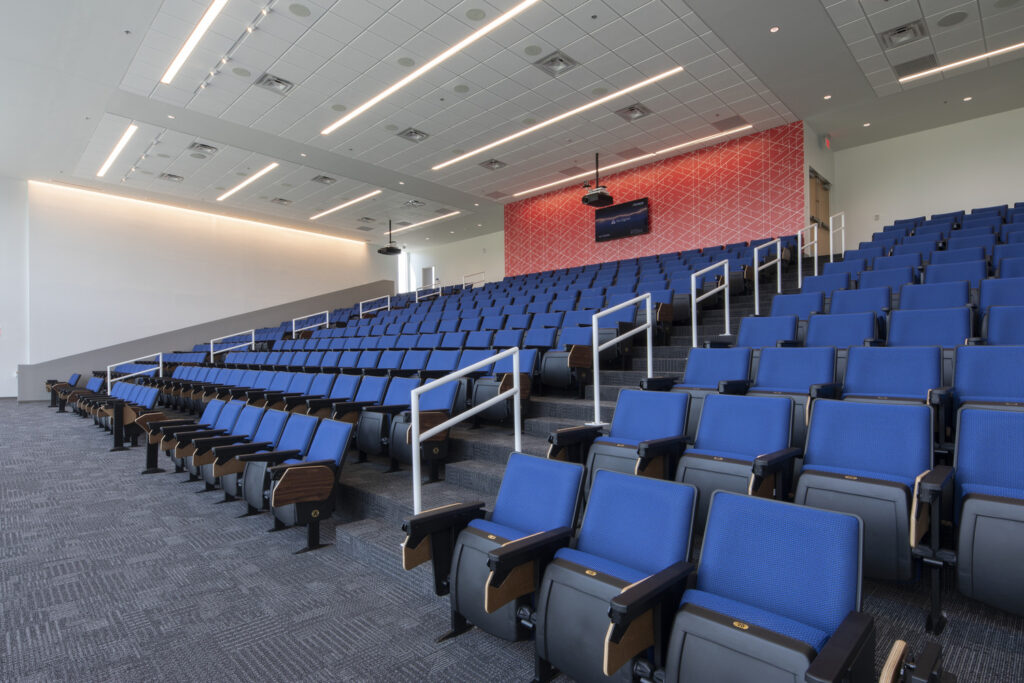 A modern lecture hall at the Alabama School of Cyber Technology and Engineering, with tiered seating and blue chairs.