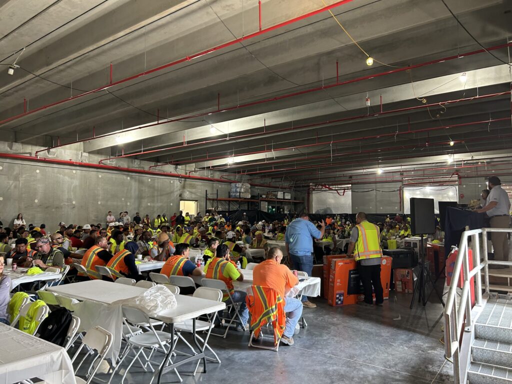 A group of construction workers from Brasfield & Gorrie attending a meeting in a large industrial space as the Texas Data Center tops out.