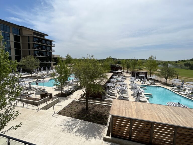 Modern apartment complex with an outdoor swimming pool and lounge area on a sunny day in Texas.