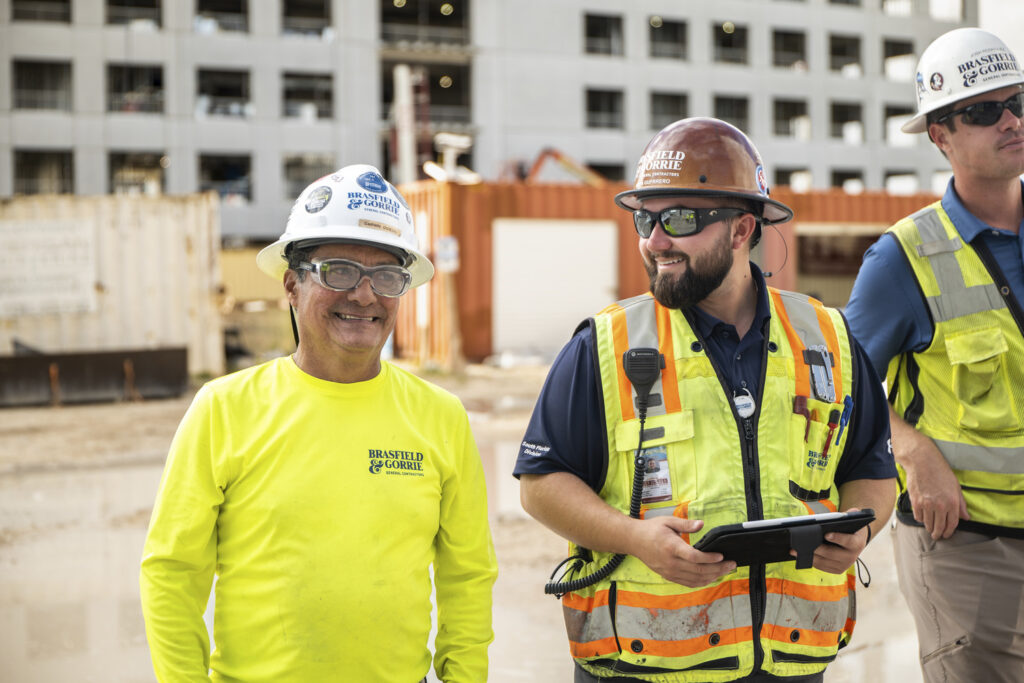 Two construction workers in reflective vests and hard hats are improving jobsite efficiency at a Procore-managed construction site.