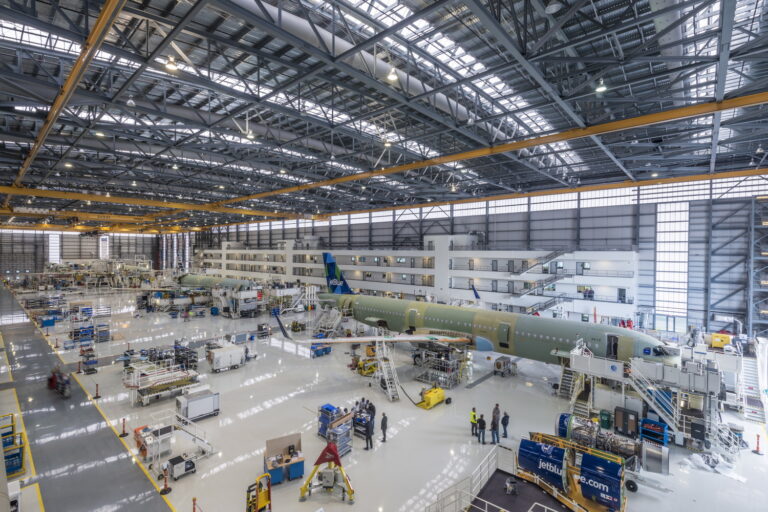 An expansive aerospace engineering hangar with workers and various sections of airplanes under construction.