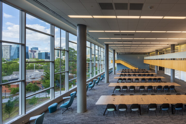 Modern commercial library interior with large windows offering a city view, featuring study tables and casual seating areas.