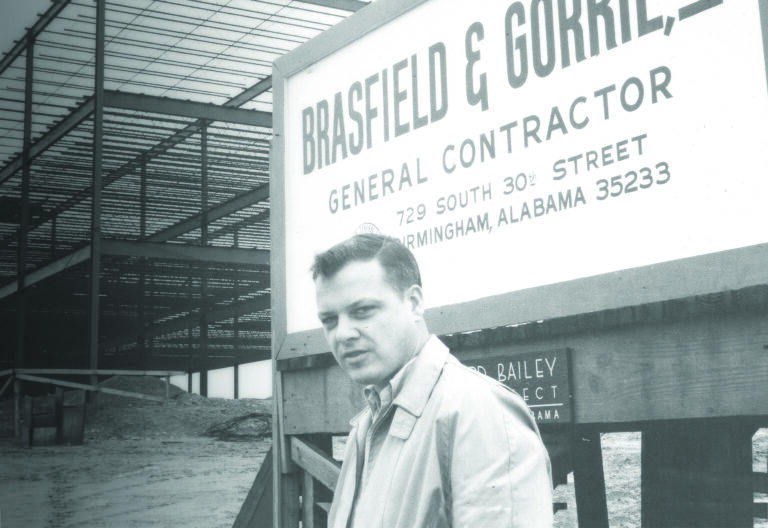 A vintage photo of a man standing in front of a sign.
