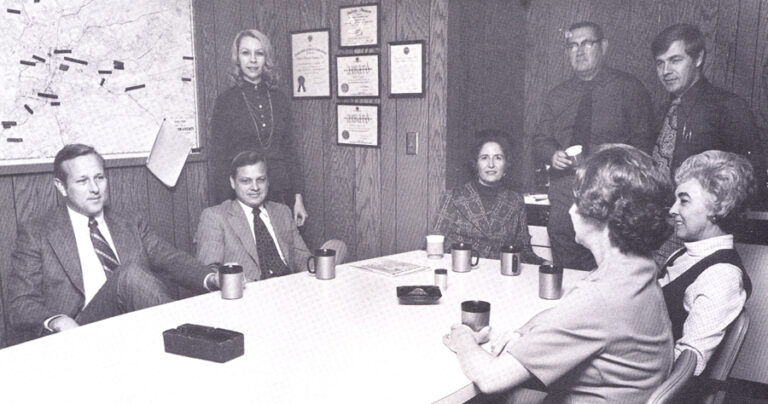 A vintage photo of a group of people sitting around a table.