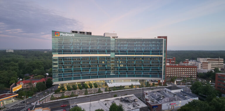 Aerial view of a large hospital building in the Healthcare supersector with the Piedmont logo at twilight.