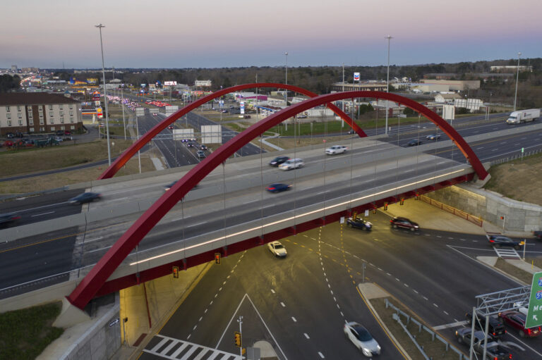 Aerial view of a red arch pedestrian bridge over a busy highway intersection at dusk, symbolizing the connection between network security and our daily travels.