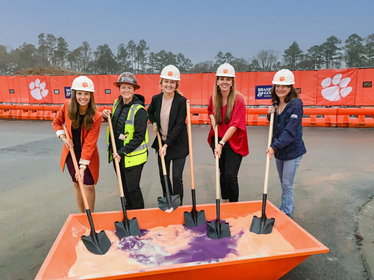 Five individuals wearing hard hats and holding shovels at a groundbreaking ceremony.