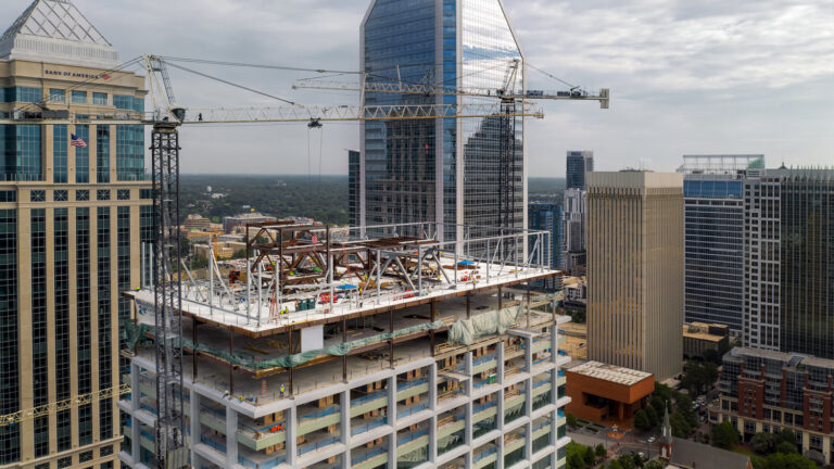 High-rise building under construction with cranes in Charlotte, NC, surrounded by cityscape.
