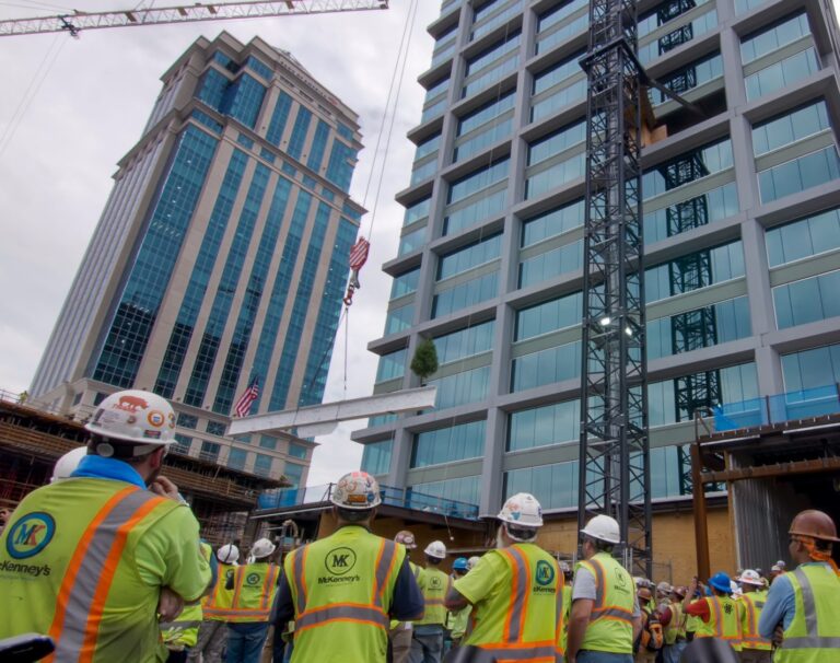 Construction workers in safety gear observing a construction site with cranes and high-rise buildings in the background in Charlotte, NC.